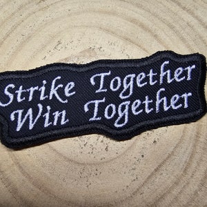 May include: Black embroidered patch with white text that reads "Strike Together Win Together".