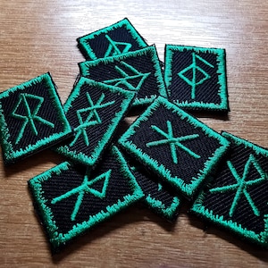 May include: A collection of ten black fabric patches with green embroidered edges. Each patch features a different Norse rune symbol.