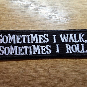 Peut inclure: Écusson brodé noir avec du texte blanc qui dit "Sometimes I walk, Sometimes I roll."
