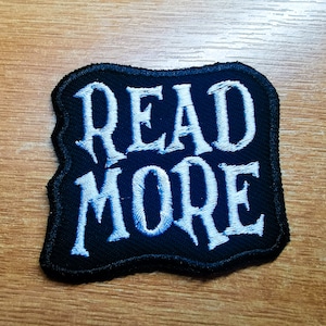 May include: A black embroidered patch with white stitching that reads "READ MORE".