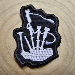Puede incluir: Un parche bordado blanco de una gaita sobre un fondo negro.