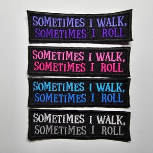 Puede incluir: Cuatro parches bordados con el texto "SOMETIMES I WALK, SOMETIMES I ROLL". Los parches son negros con el texto en morado, rosa, azul y blanco. Los parches son rectangulares con la parte superior e inferior curvadas.