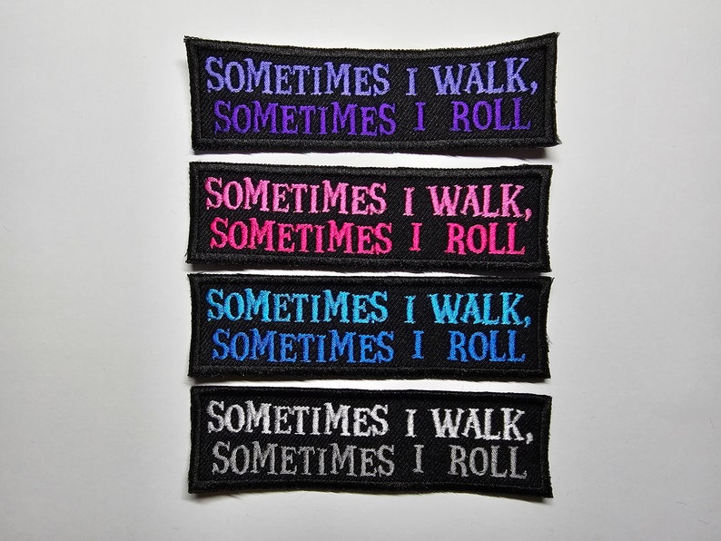 Puede incluir: Cuatro parches bordados con el texto "SOMETIMES I WALK, SOMETIMES I ROLL". Los parches son negros con el texto en morado, rosa, azul y blanco. Los parches son rectangulares con la parte superior e inferior curvadas.