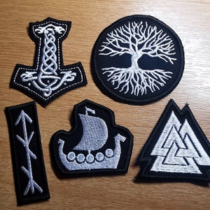 Puede incluir: Seis parches bordados termoadhesivos con temática nórdica. Los parches son blancos sobre tela negra. Los diseños incluyen un barco vikingo, un árbol de la vida, un martillo, un Valknut y dos flechas.