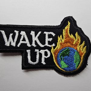 May include: Black embroidered patch with white text that reads "WAKE UP" and a globe on fire. The globe is blue, green, and yellow.