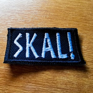 May include: A black embroidered patch with white stitching that reads "SKÅL!"