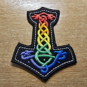 May include: A rainbow-colored embroidered patch in the shape of a Viking hammer, or Mjolnir, with a white outline.