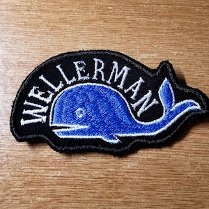 May include: A black and white embroidered patch with a blue whale and the text "WELLERMAN" in white.
