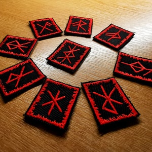 May include: A collection of ten black embroidered patches with red stitching. Each patch features a unique red rune symbol. The patches are square or rectangular with a red border, arranged on a wooden surface.