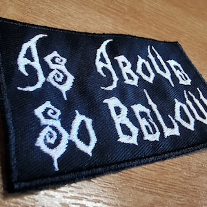 May include: Black embroidered patch with white lettering that reads "As Above So Below".