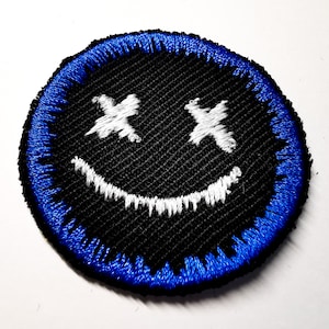 May include: A black and blue embroidered patch with a white smiley face with X's for eyes.