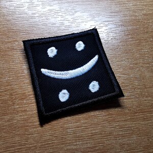 May include: Black fabric patch with a white embroidered smiley face.