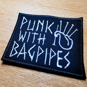 Może przedstawiać: Czarna naszywka haftowana białymi nićmi. Naszywka zawiera napis "Punk with Bagpipes" i przedstawia stylizowany wizerunek dud.