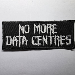 Puede incluir: Un parche rectangular negro con texto bordado en blanco que dice "NO MORE DATA CENTRES". El texto tiene un estilo de fuente gótica y dentada. El parche está diseñado para ser cosido o planchado en ropa o accesorios.