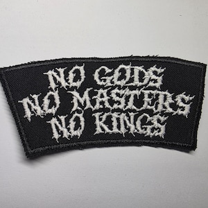 Può includere: Toppa ricamata nera con le parole bianche "NO GODS NO MASTERS NO KINGS" in caratteri gotici. La toppa ha una forma rettangolare con il bordo superiore curvo.