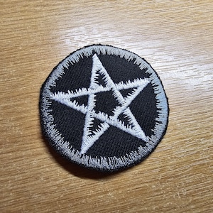 Könnte beinhalten: Ein gestickter Patch in Schwarz und Weiß mit einem fünfzackigen Stern in der Mitte. Der Stern ist weiß und der Hintergrund ist schwarz. Der Patch ist rund und hat einen grauen Rand.