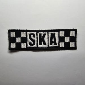 Peut inclure: Écusson brodé noir et blanc avec le mot "SKA" en lettres blanches. Le patch a une bordure noire et un motif en damier à chaque extrémité. De forme rectangulaire.