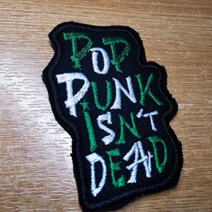 May include: Green and white embroidered patch with the text "Pop Punk Isn't Dead" on a black background.