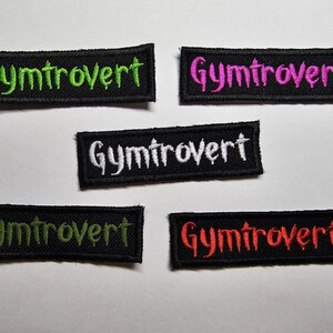 Puede incluir: Cinco parches termoadhesivos negros con la palabra "Gymtrovert" en diferentes colores: verde, rosa, blanco, verde y rojo.