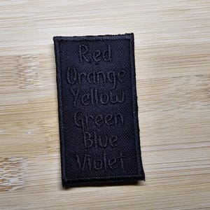 May include: Black fabric patch with the words "Red", "Orange", "Yellow", "Green", "Blue", and "Violet" embroidered in white.