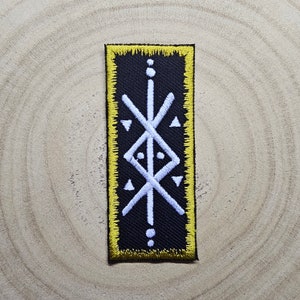 May include: A black embroidered patch with a white geometric design. The patch has a yellow border and is rectangular in shape.
