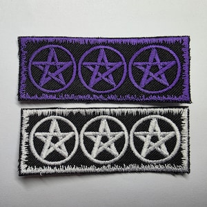 May include: Two rectangular embroidered patches featuring three pentagrams each. The top patch has purple thread on a black background with a purple border. The bottom patch has white thread on a black background with a white border.
