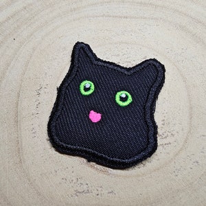 Può includere: Toppa di feltro nero a forma di viso di gatto con occhi verdi e naso rosa.