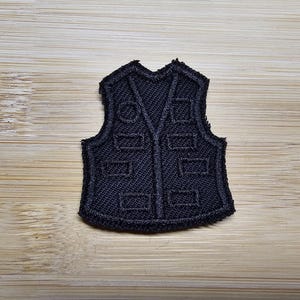 Puede incluir: Parche de chaleco bordado en negro con un diseño detallado.