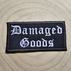 May include: Black embroidered patch with white text that reads "Damaged Goods" in a gothic font.