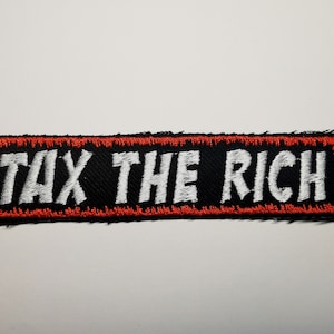 Puede incluir: Un parche bordado negro y rojo con el texto "TAX THE RICH" en blanco.