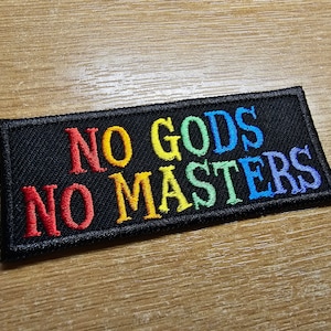 May include: A black fabric patch with the words "NO GODS NO MASTERS" embroidered in rainbow colors.