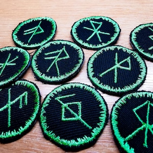 Könnte beinhalten: Acht schwarze und grüne gestickte Patches mit verschiedenen Runen auf jedem. Die Runen sind in einem grünen Umriss auf schwarzem Hintergrund.