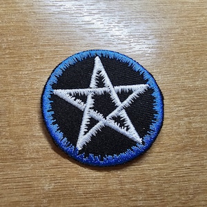 May include: A white five-pointed star with a blue outline, embroidered on a black circle patch.
