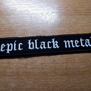 May include: Black fabric patch with white embroidered text that reads "epic black metal".