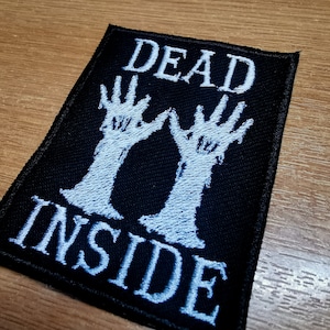 Op de afbeelding: Zwarte stoffen patch met witte borduurwerk. De patch heeft twee skeletachtige handen die omhoog reiken en de tekst "DEAD INSIDE".