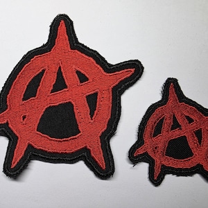 Op de afbeelding: Twee geborduurde patches met het anarchie-symbool. De grotere patch is ongeveer 7,6 cm breed en de kleinere ongeveer 5 cm. Beide hebben een rood symbool op een zwarte achtergrond met een zwarte rand.