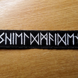 May include: Black embroidered patch with white text that reads "SNIMMANAMN".