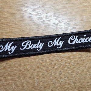 May include: Black embroidered patch with white cursive text that reads "My Body My Choice".
