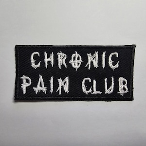 Könnte beinhalten: Schwarzer rechteckiger Aufnäher mit weiß gesticktem Text "CHRONIC PAIN CLUB". Der Text ist übereinander angeordnet, mit einer verformten, leicht gezackten Schriftart. Der Aufnäher hat ein schlichtes, kühnes Design.