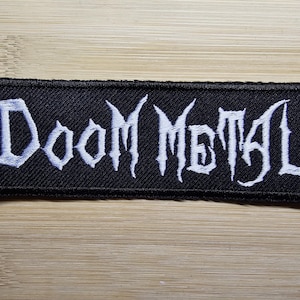 May include: Black fabric patch with white embroidered text that reads "Doom Metal".