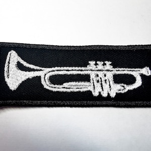 以下が含まれることがあります： 黒い布のパッチに白い刺繍のトランペットが施されています