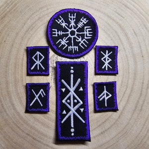 May include: Set of eight embroidered iron-on patches featuring Norse symbols, including a Vegvisir compass, a rune for protection, and a rune for strength. The patches are black with white embroidery and have a purple border.