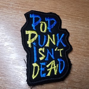 May include: A black embroidered patch with the text "Pop Punk Isn't Dead" in yellow and blue thread.