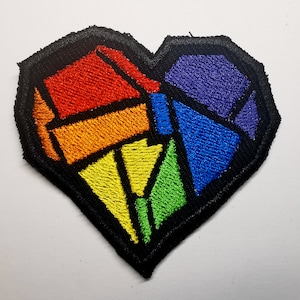 May include: A rainbow-colored heart-shaped patch with a geometric design. The patch is made of embroidered fabric and has a black outline.