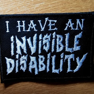 Könnte beinhalten: Schwarzer Stoff-Patch mit weiß gesticktem Text, der "Ich habe eine unsichtbare Behinderung" lautet.