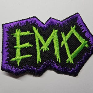 May include: Green embroidered letters spelling "EMO" on a black fabric patch with a purple border.