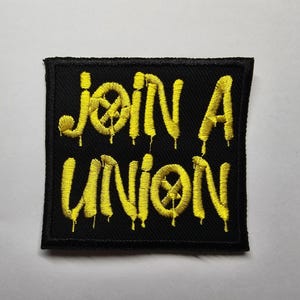 Könnte beinhalten: Schwarzer, gestickter Aufnäher mit gelbem Text, der "JOIN A UNION" lautet. Der Text hat einen Tropfeffekt. Der Aufnäher ist quadratisch mit einem schwarzen Rand.