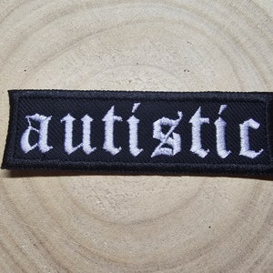 Peut inclure: Patch en tissu noir avec du texte brodé blanc qui dit "autistique" dans une police gothique.