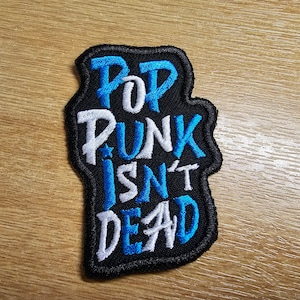 May include: A black embroidered patch with the text "Pop Punk Isn't Dead" in white and blue lettering.