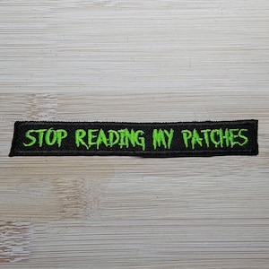 May include: Black and green embroidered patch with the text "STOP READING MY PATCHES" in a dripping font.